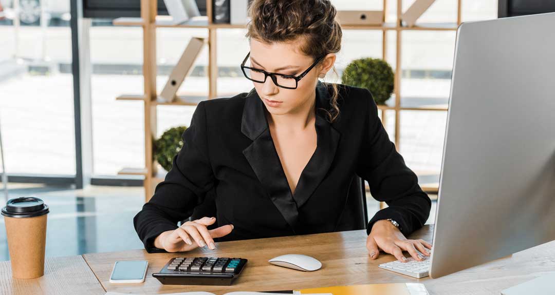 a woman sitting at her office desk using a calculator