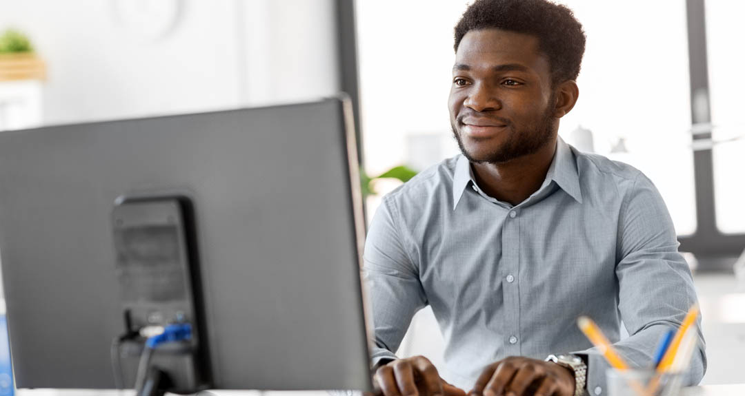 This is an image of a Black man with a grey button down shirt looking at a computer.