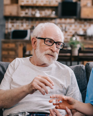 A nurse gives an elderly man his medicine in his home. 