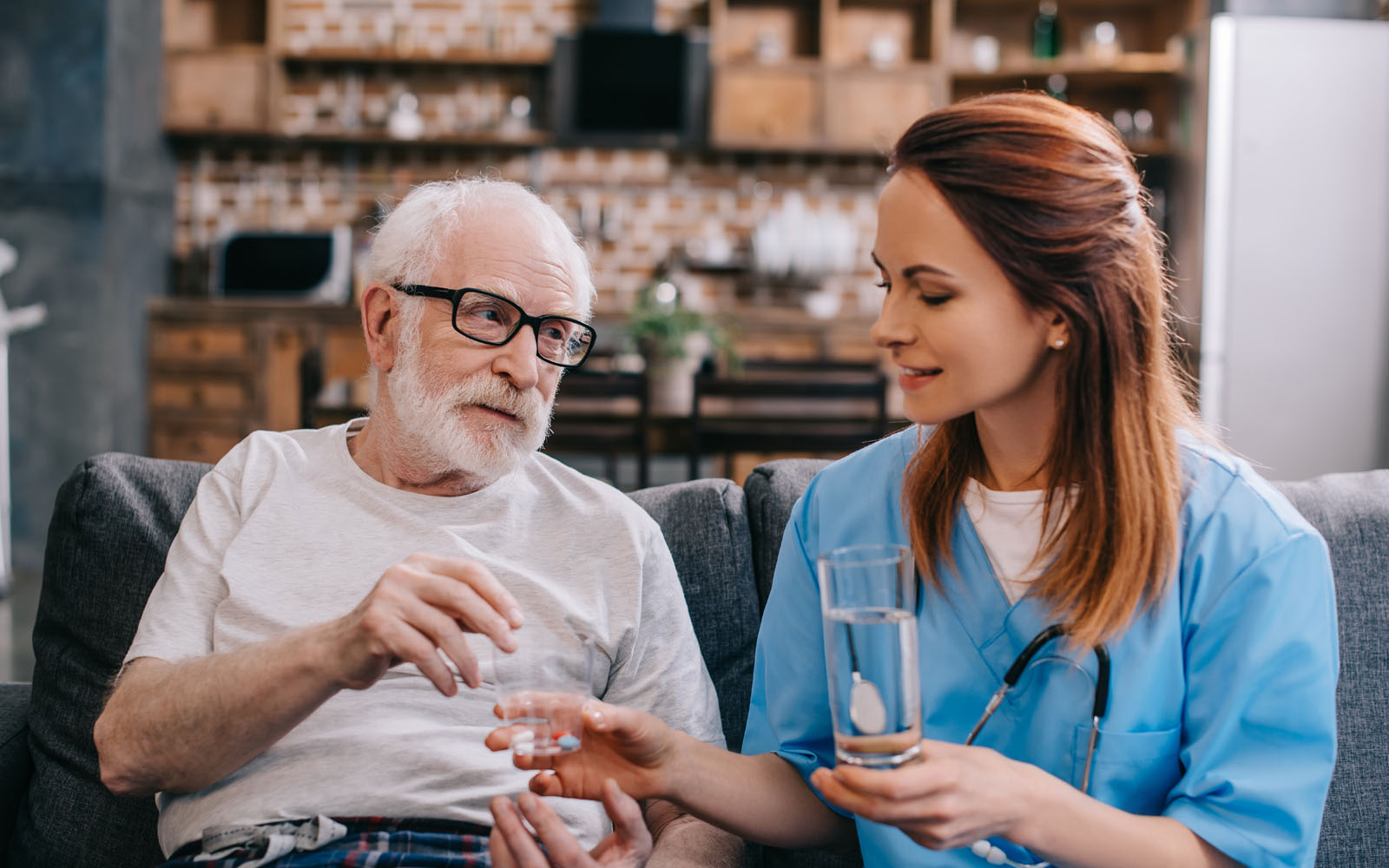 A nurse gives an elderly man his medicine in his home. 
