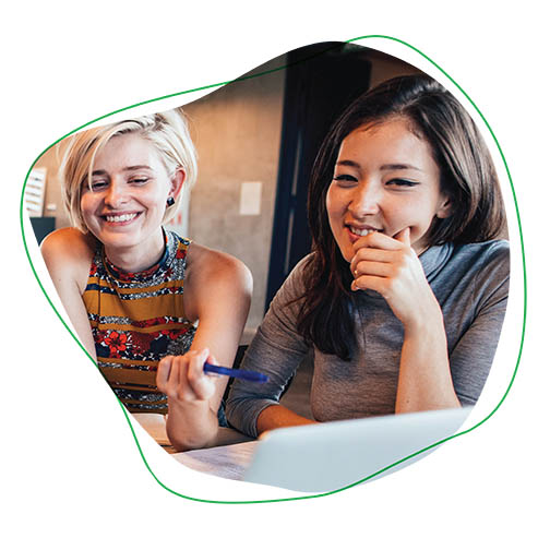 Two students -- a blond girl and a brunette girl, smile at their computer.