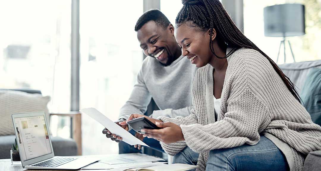 a couple in their living room reviewing finances on a calculator and laptop