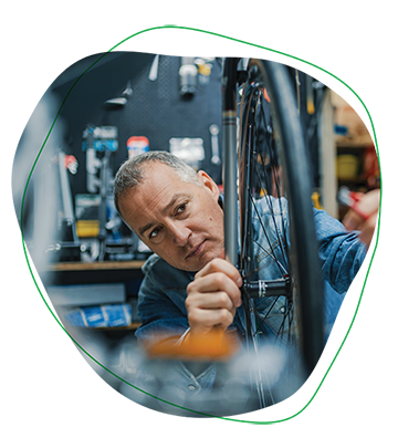 This is a photograph within a freeform element of a man in a bike shop fixing a tire.