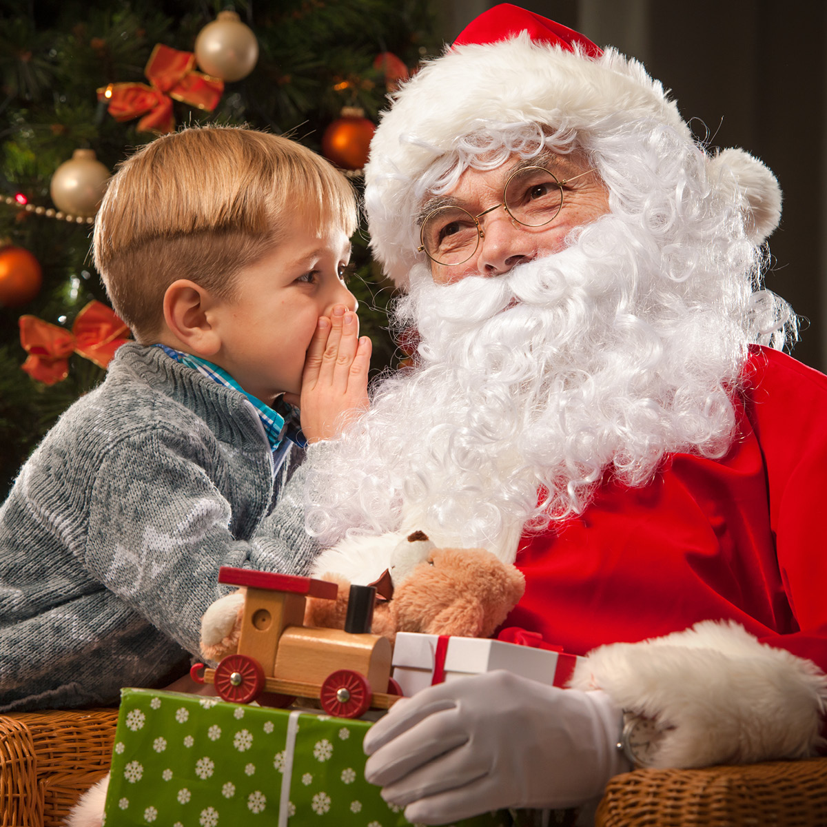photo of a little child whispering into Santa Claus' ear.