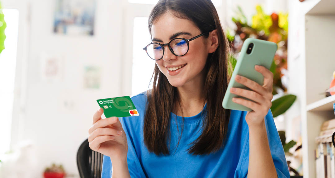 A brown haired female student holds her phone and a GSB debit card.
