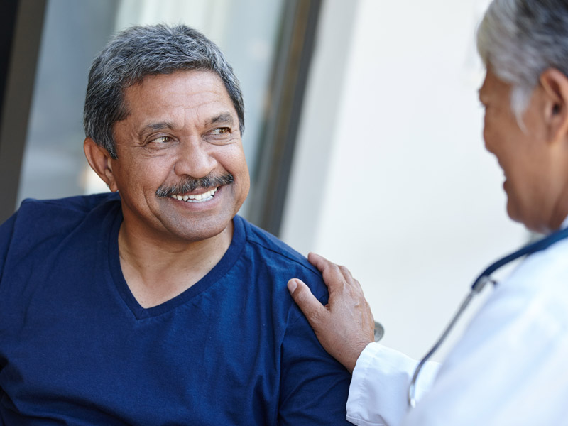 Senior man smiles while comforted by healthcare worker