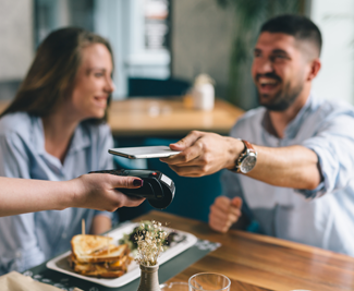 Smiling man at restaurant holding out his phone to tap to pay.