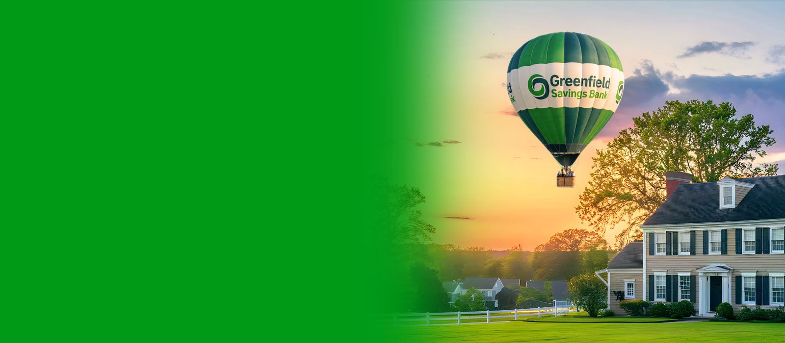 Photo of a hot air balloon with the Greenfield Savings Bank logo, hovering over a house at sunset.