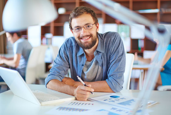 a man at his desk with a laptop and financial charts and graphs